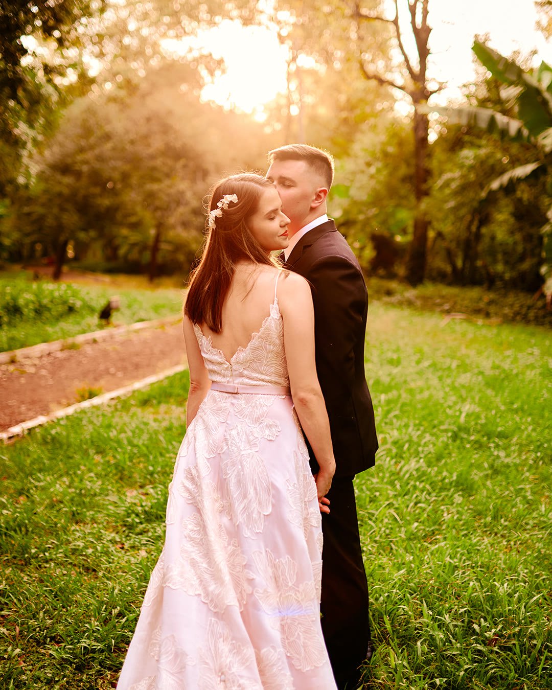 Novios abrazados de espaldas a contraluz, en un parque con el sol bajando entre los árboles