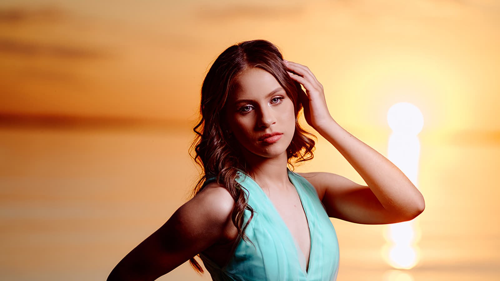 Quinceañera con vestido celeste frente al atardecer sobre el agua en Encarnación