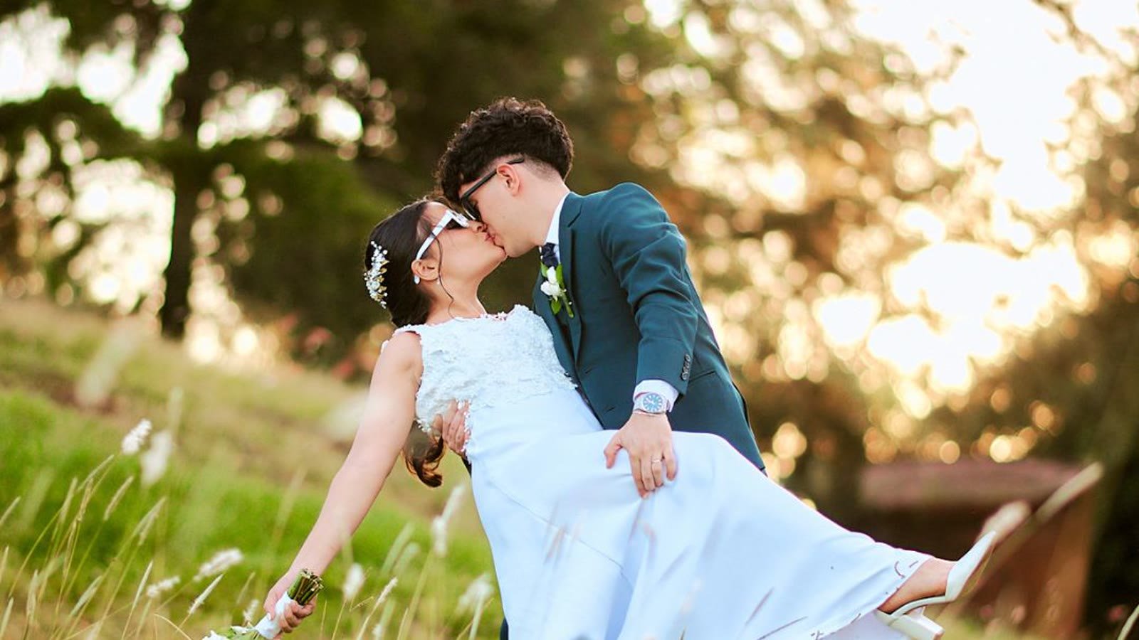 Novios besándose en un campo al atardecer, con el vestido al viento