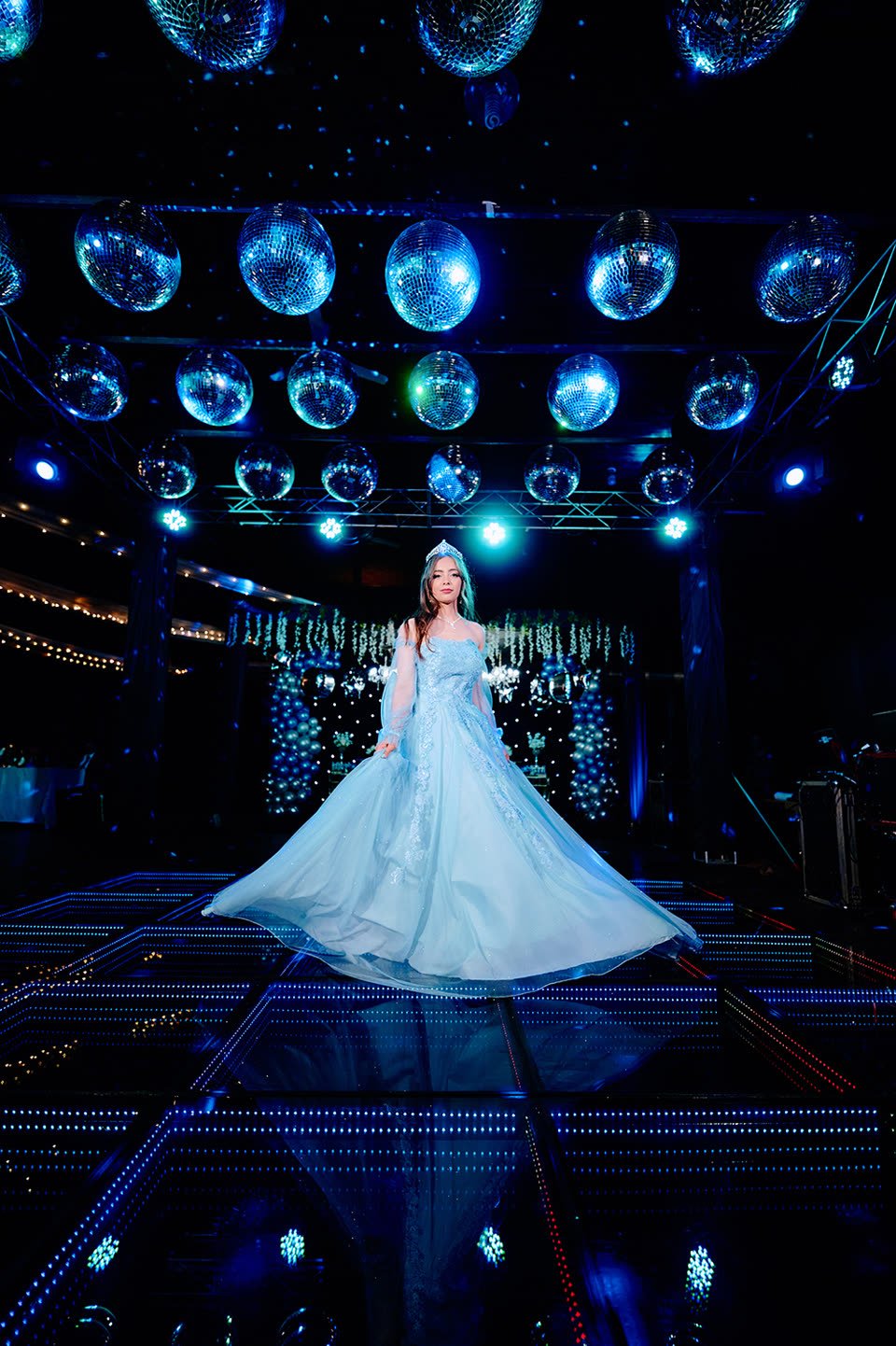 Quinceañera con vestido celeste girando en la pista iluminada de su fiesta