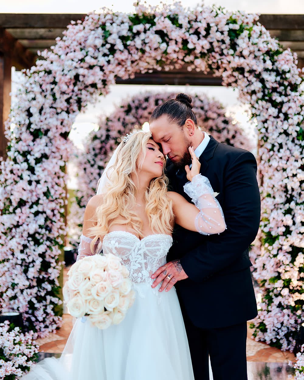Novios abrazados bajo un arco de flores blancas en su boda en Encarnación