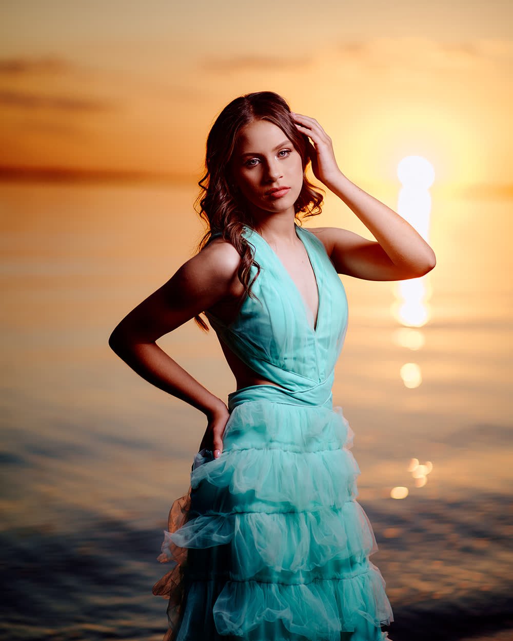 Retrato de una quinceañera con vestido turquesa frente al río al atardecer