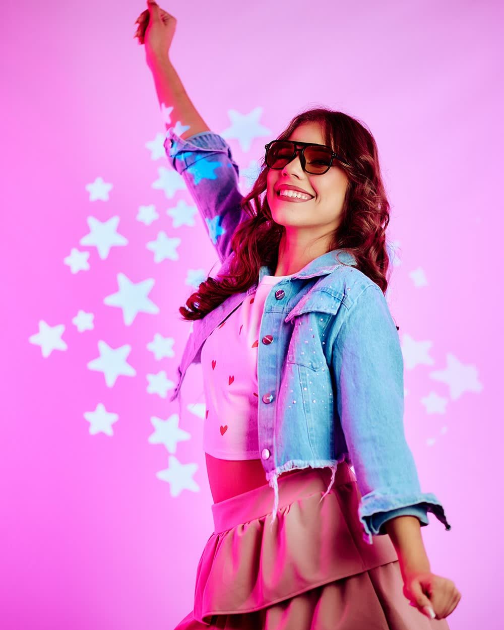 Chica con campera de jean y lentes de sol sobre fondo rosa con estrellas en su sesión pre-xv