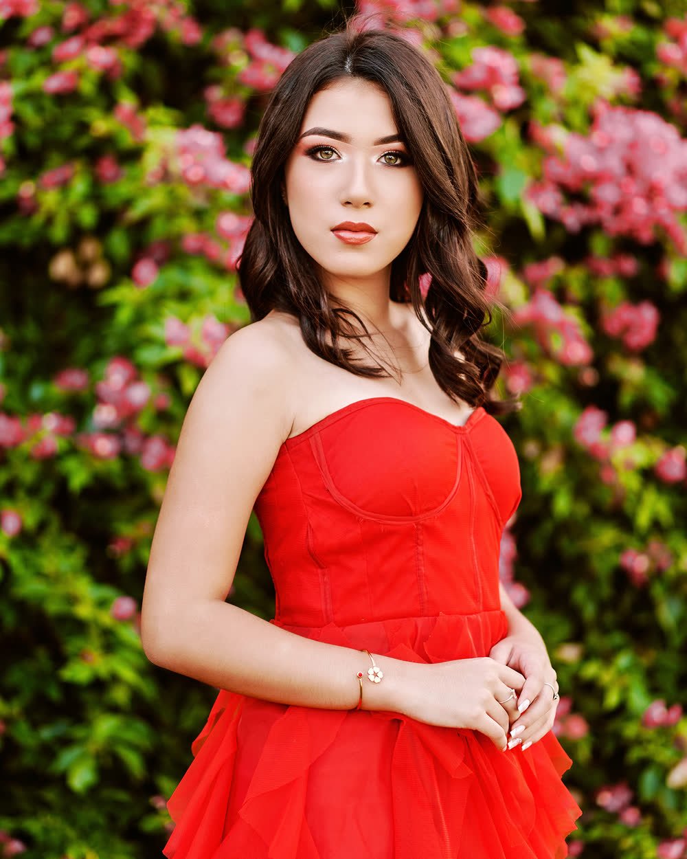 Quinceañera con vestido rojo entre flores rosas en su sesión pre-xv
