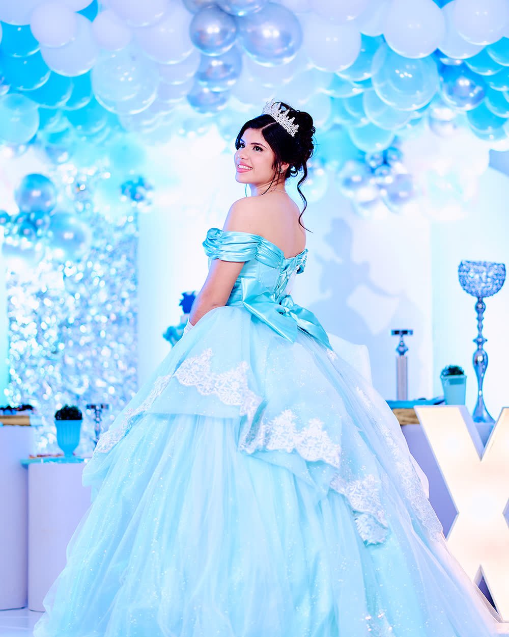 Quinceañera con vestido celeste frente a una pared de globos