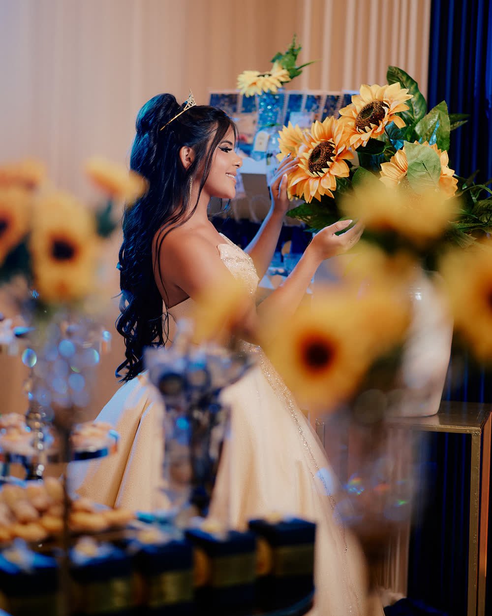 Quinceañera con vestido dorado acomodando girasoles en la mesa de su fiesta