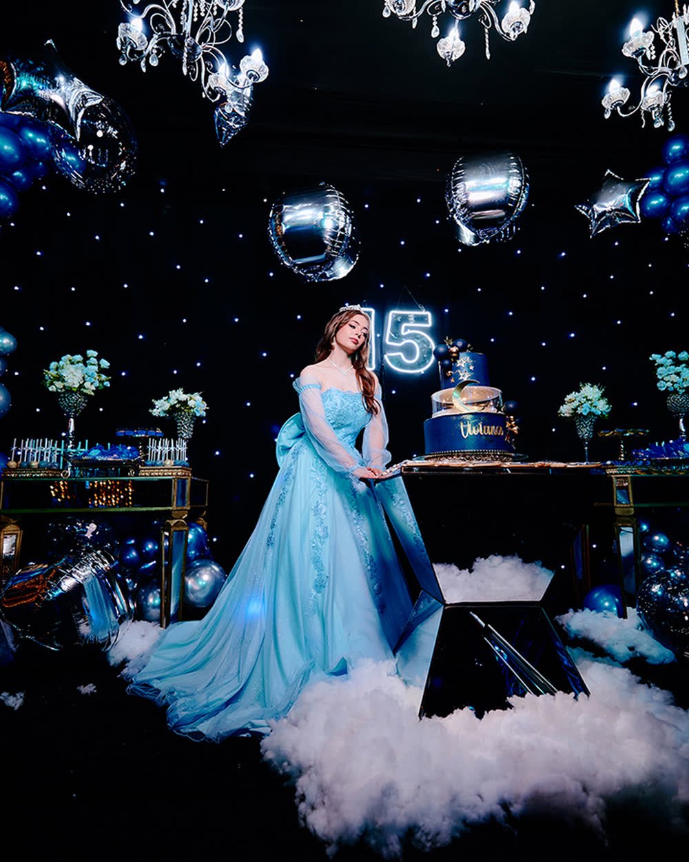 Quinceañera con vestido celeste entrando entre humo junto a su torta de 15