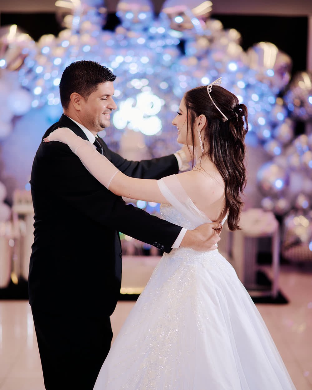 Quinceañera bailando el vals con su padre bajo un techo de globos